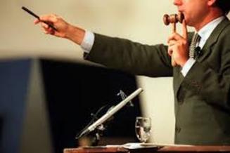 A man in a suit holding a gavel and pointing to the side.