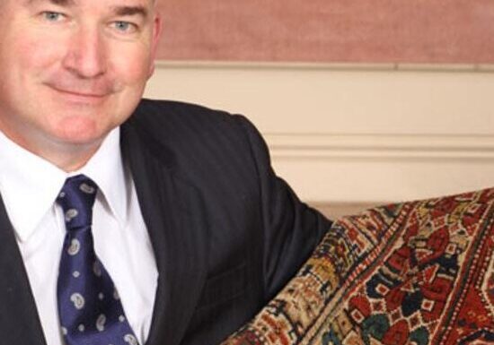 A man in a suit holding a patterned carpet. A man in a suit holding a patterned carpet.