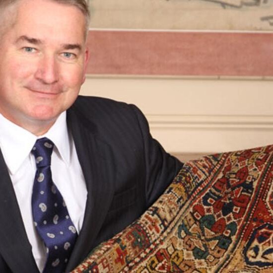 A man in suit and tie holding onto a rug.