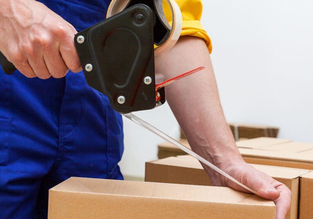 A person packing boxes using tape in a work setting. A person packing boxes using tape in a work setting.